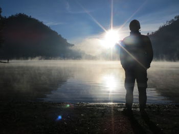 Rear view of silhouette man standing at shore against sky