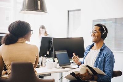 Cheerful male computer hacker talking with female coworker while sitting at desk in creative office