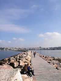 People sitting on rock by sea against sky