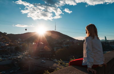 Woman sitting on railing against cityscape during sunset