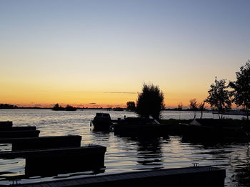 Silhouette trees by sea against clear sky during sunset