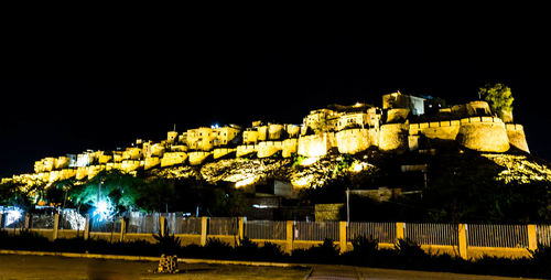 Illuminated street light by building against sky at night