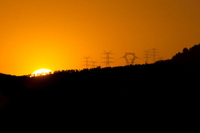 Silhouette electricity pylons on land against sky during sunset