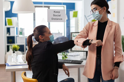 Businesswomen wearing mask bumping elbow at office