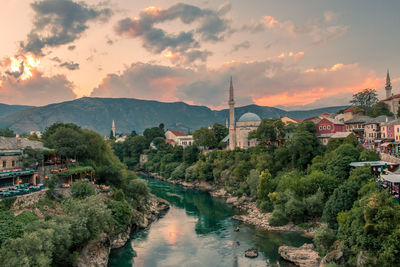 River amidst trees against cloudy sky in town during sunset