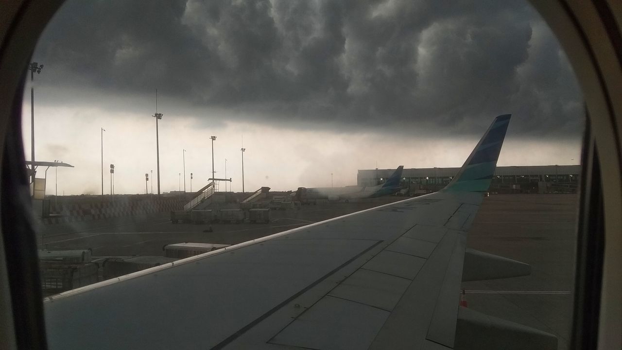 AIRPLANE ON RUNWAY AGAINST SKY SEEN THROUGH GLASS WINDOW