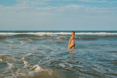 Rear view of woman standing at beach against sky