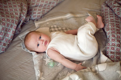 Newborn baby is lying on a bed in a white knitted jumpsuit