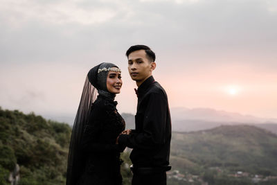 Young couple standing against sky during sunset