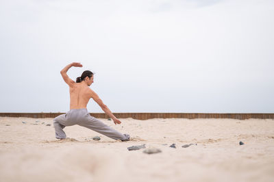 Full length of woman doing yoga at beach against sky