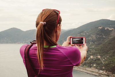 Rear view of woman photographing mountains against sky