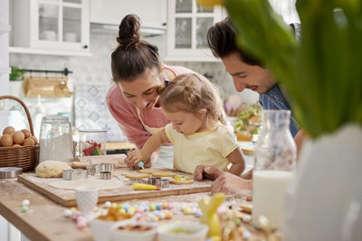 Father by mother and daughter preparing food in kitchen