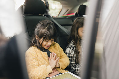 Smiling girl using digital tablet while sitting in car