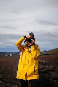 Rear view of woman photographing with camera while standing against sky