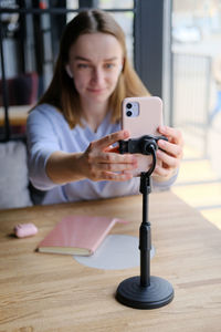 Young beautiful woman blogger making a video for her blog using phone camera in a cafe.