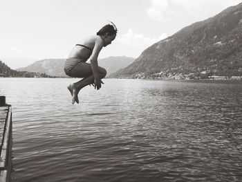 Full length of shirtless man jumping in lake against sky