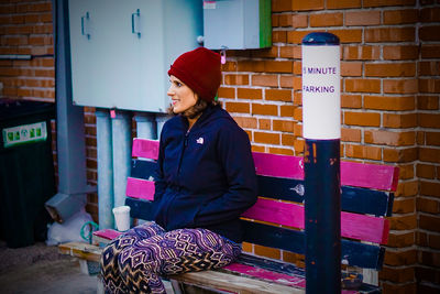 Happy woman with hands in pockets sitting on bench