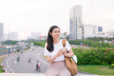 Smiling woman using mobile phone while standing in city