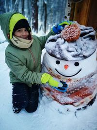 Portrait of cute boy kneeling by snowman