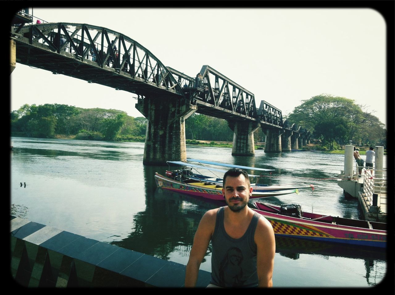 water, lifestyles, young adult, person, bridge - man made structure, leisure activity, transfer print, clear sky, river, portrait, connection, built structure, architecture, looking at camera, railing, casual clothing, auto post production filter, standing