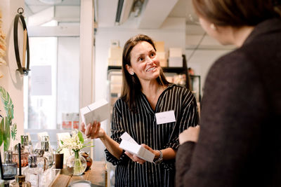 Smiling saleswoman with perfume box talking to customer at store