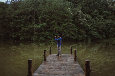 Man standing on pier over lake in forest