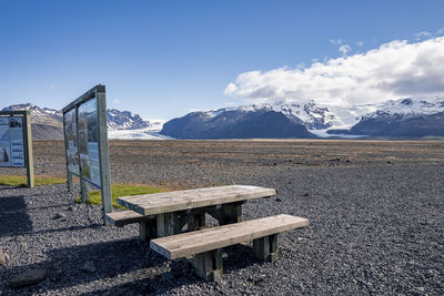 Wooden benches by information signboards with snowcapped mountains in background