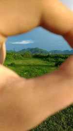 Close-up of hand on green field against sky