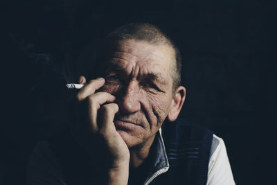 Close-up portrait of man smoking cigarette against black background