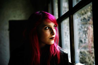 Beautiful woman with dyed hair looking through window at home