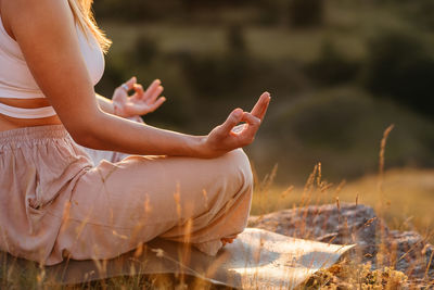 Unrecognisable woman connecting fingers on hands while sitting on mat, concept of meditation outdoor