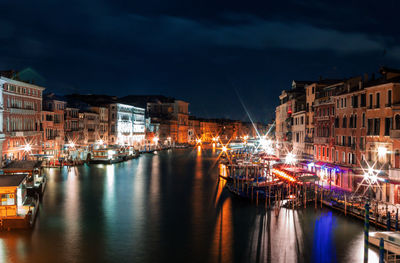 Boats moored at harbor by buildings against sky at night