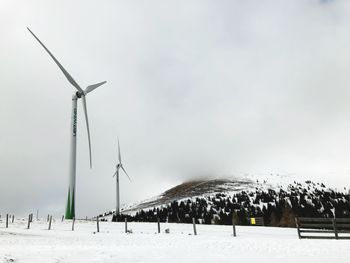 Wind turbines on snow covered field against sky