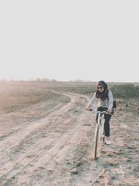 Full length of woman riding bicycle on land against clear sky during sunset