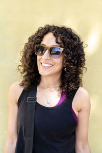 Portrait of young woman wearing sunglasses standing against yellow wall