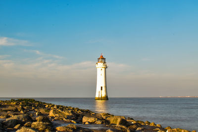 Lighthouse amidst sea and buildings against sky