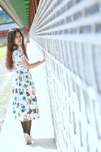 Portrait of young woman smiling while standing by wall