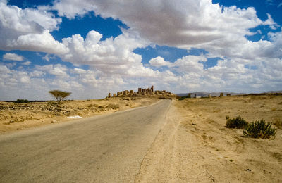 Dirt road amidst desert against sky