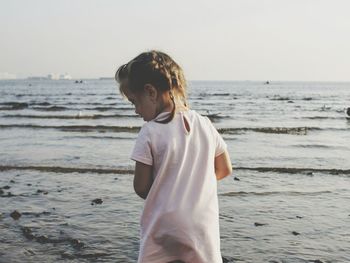 Rear view of girl standing at beach during sunset