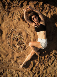 Full length of woman lying by bitcoin symbol at beach