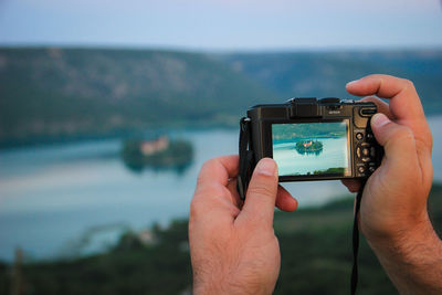 Cropped image of man hands photographing lake with camera