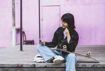 Smiling teenage girl using mobile phone in front of wall