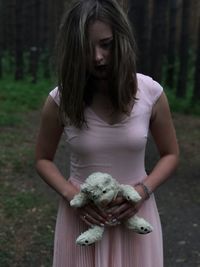 Young woman holding teddy bear while standing in forest