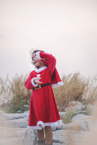 Girl wearing red dress while standing on rocks against sky during christmas