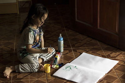 Full length of girl painting in paper while sitting on floor at home