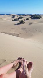 Low section of person on sand at beach against sky