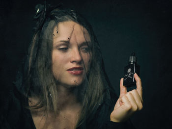 Close-up of mid adult woman holding bottle against black background
