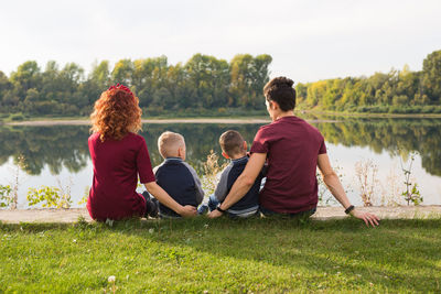 Rear view of people sitting on grass by lake