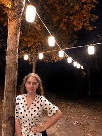 Young woman standing below illuminated lighting equipment at night