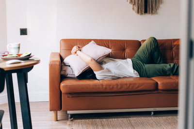 A woman lies on the sofa and covers her face with a pillow, unable to cope with the problems.